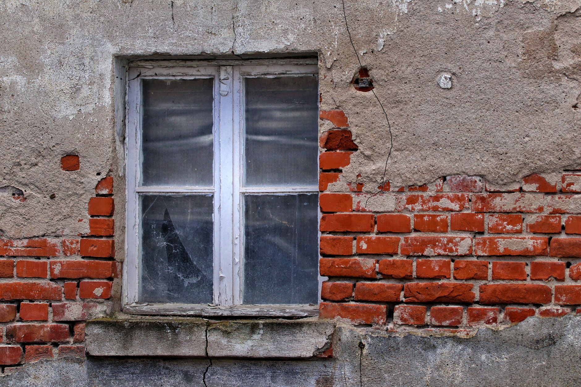 Rustic brick wall with an aged window, showcasing urban decay and architectural texture.