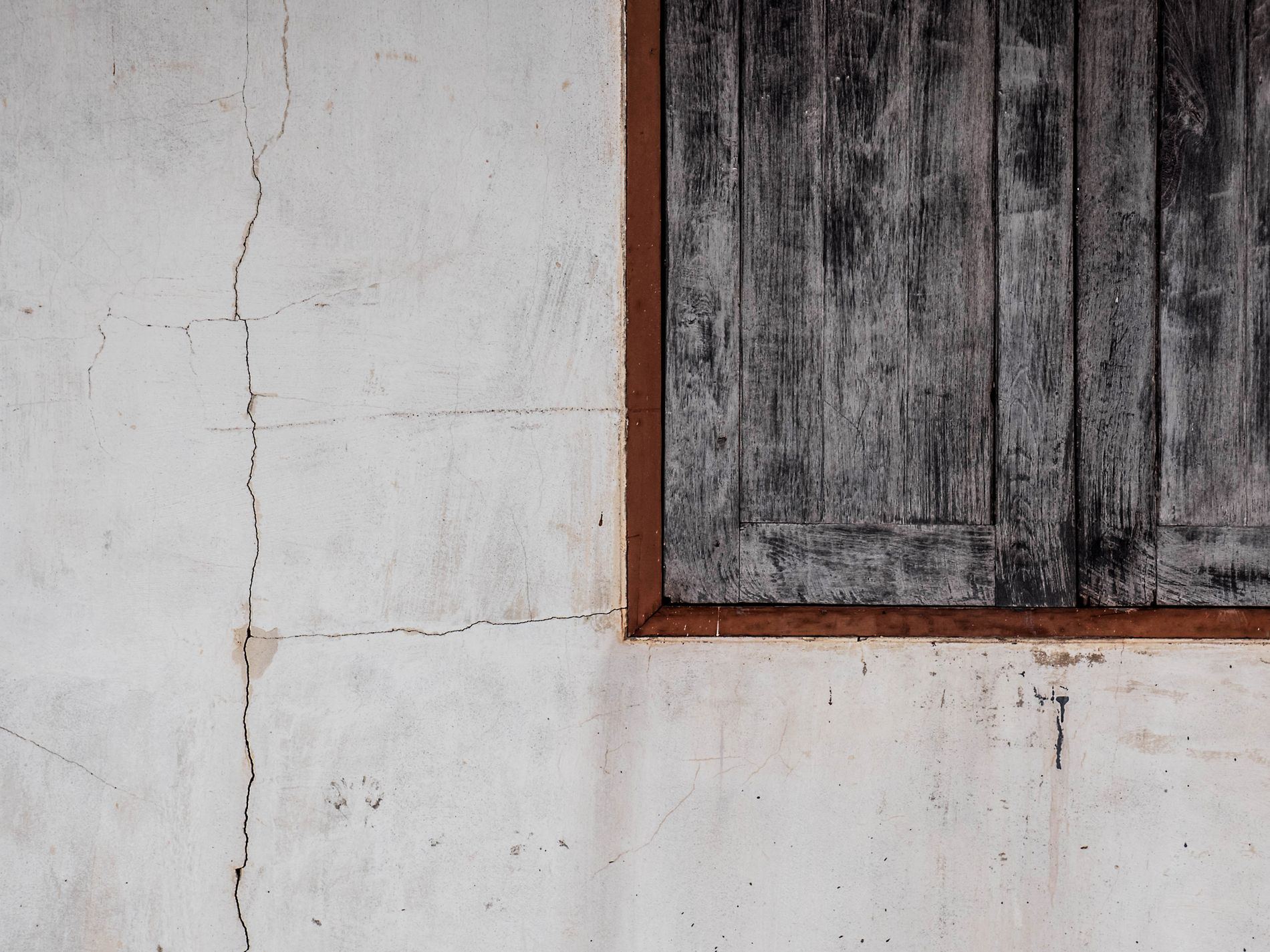 Close-up of a rustic wooden window on a cracked wall, highlighting textures and traditional design.