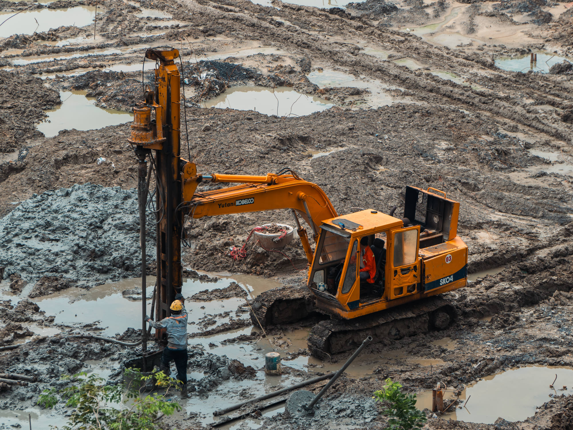 An excavator and worker on a muddy construction site showing industrial equipment.
