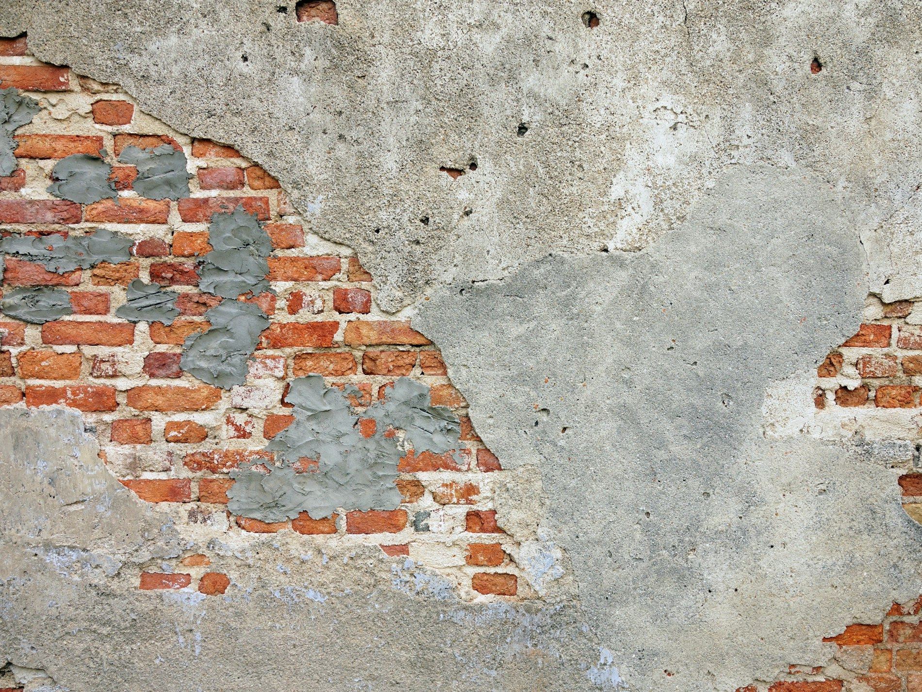 A weathered brick wall with patches of grey plaster and exposed red bricks