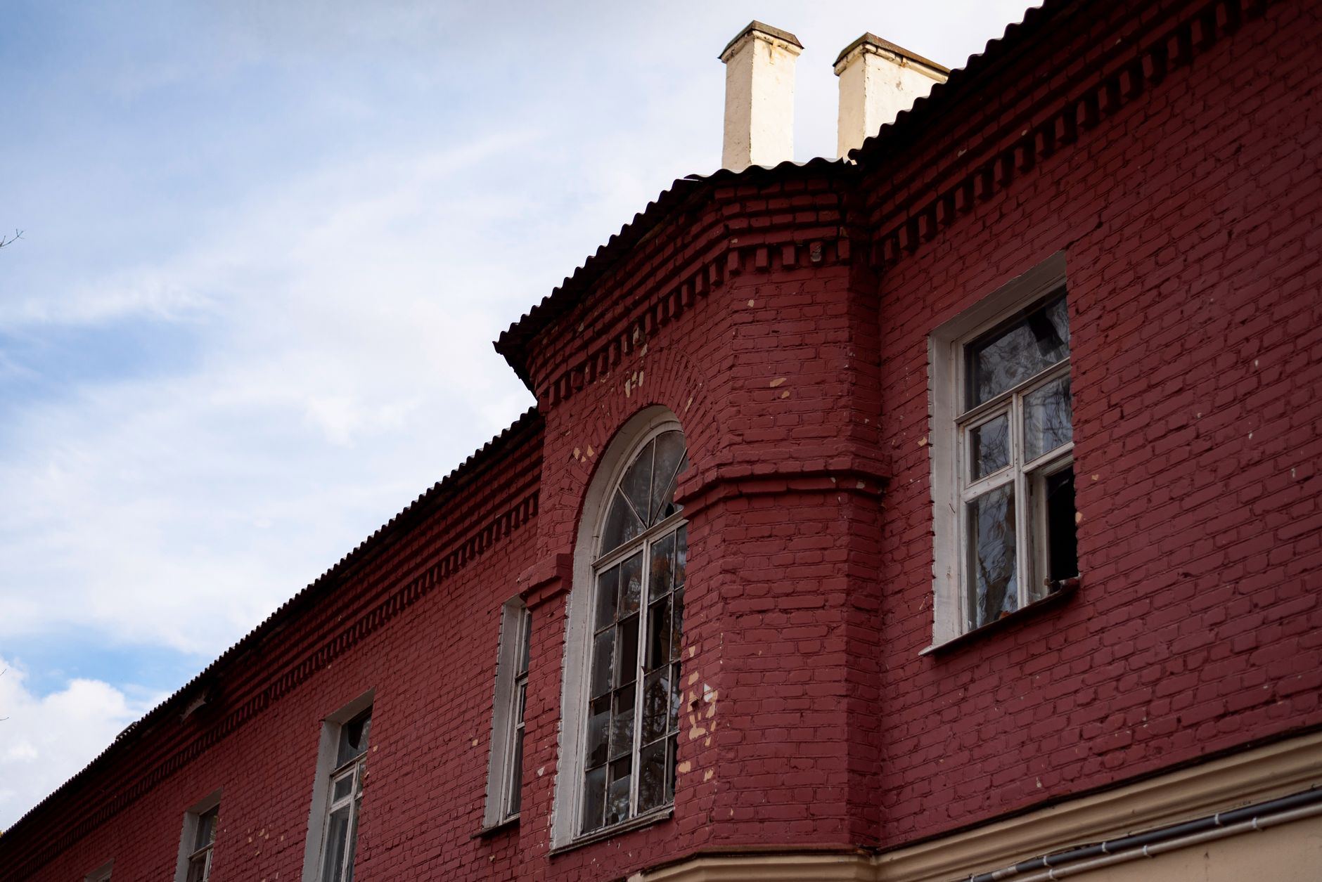 A detailed view of a red brick building facade with an arched window under a blue sky.